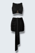 The Saint 54 black two-piece mini set featuring a fitted crop top with gold accent and a draped gathered mini skirt.