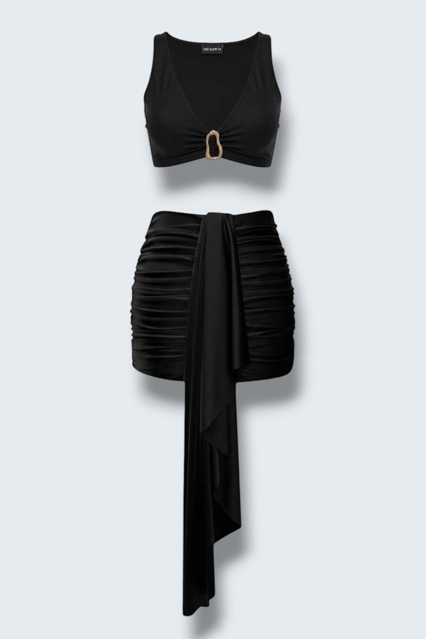 The Saint 54 black two-piece mini set featuring a fitted crop top with gold accent and a draped gathered mini skirt.