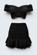 The Saint 54 black two-piece set featuring a gathered off-shoulder cropped top and a ruffled mini skirt.