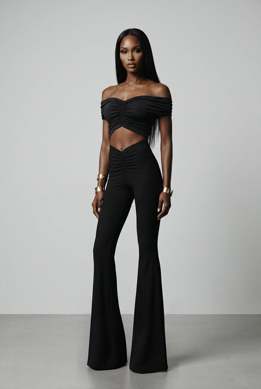The Saint 54 black two-piece set with off-shoulder ruched crop top and high-waisted wide-leg trousers on a model.