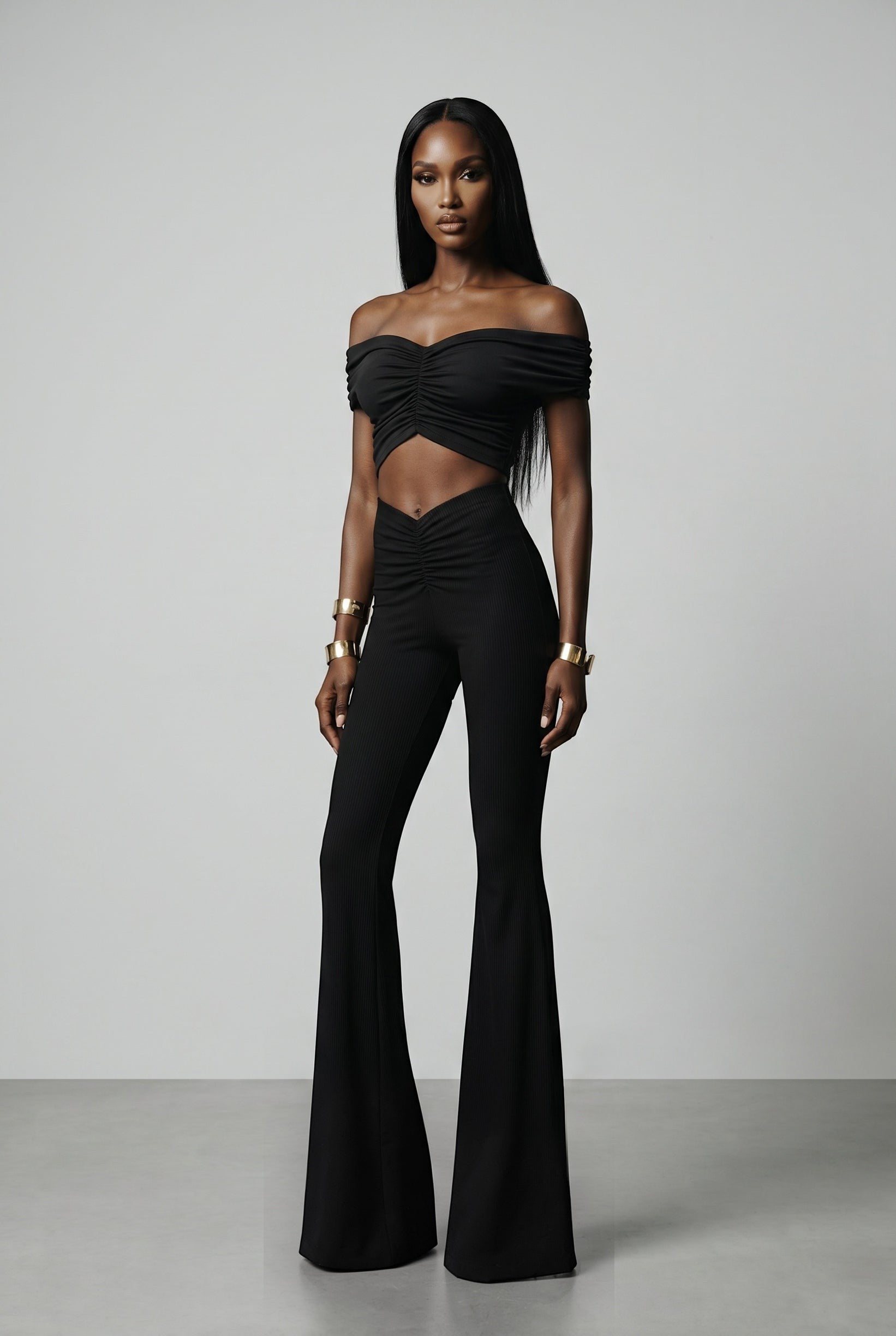 The Saint 54 black two-piece set with off-shoulder ruched crop top and high-waisted wide-leg trousers on a model.