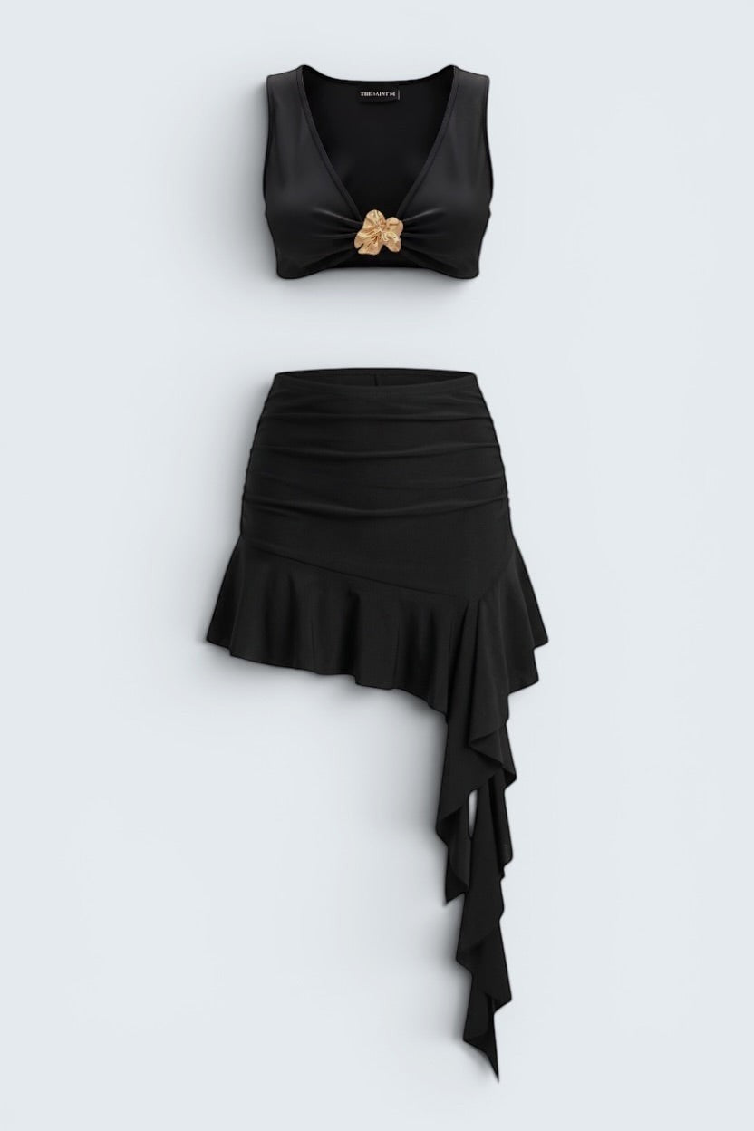 The Saint 54 black two-piece set featuring a fitted crop top with gold accent and an asymmetrical ruffled mini skirt.