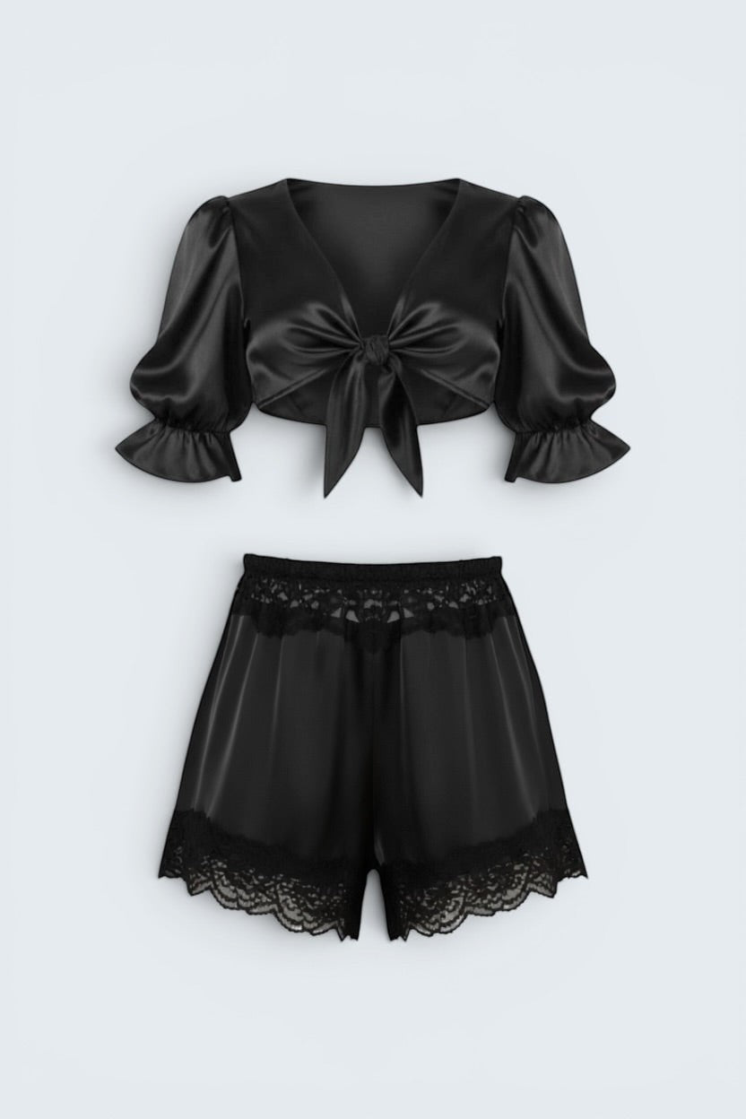 The Saint 54 black satin lounge set with a tie-front puff sleeve top and high-waisted shorts featuring lace trim.