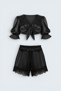 The Saint 54 black satin lounge set with a tie-front puff sleeve top and high-waisted shorts featuring lace trim.