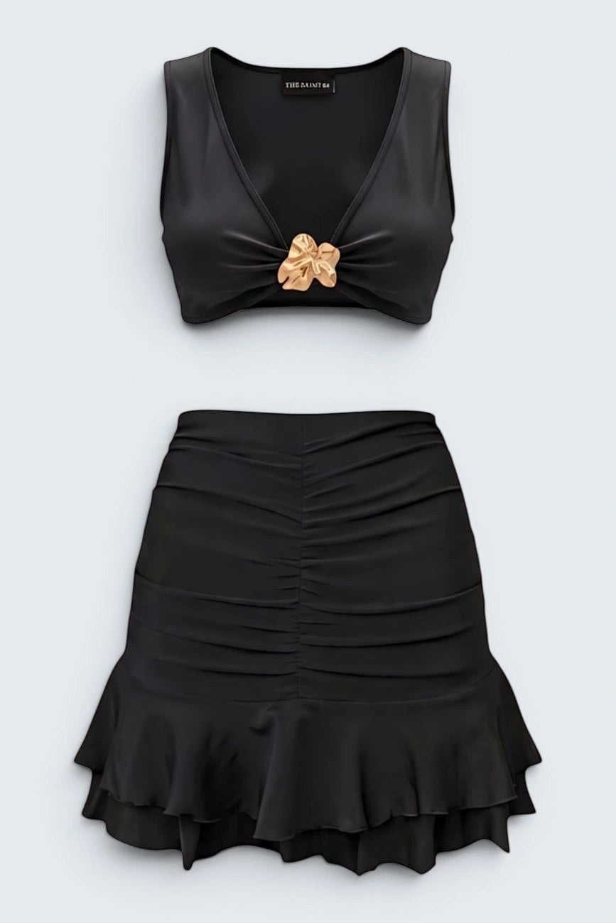 The Saint 54 black two-piece set with a fitted crop top featuring a gold accent and a ruched mini skirt with ruffled hem