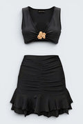 The Saint 54 black two-piece set with a fitted crop top featuring a gold accent and a ruched mini skirt with ruffled hem