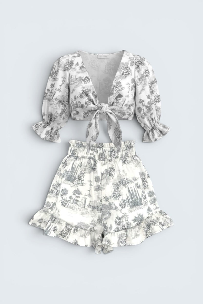 The Saint 54 grey toile print two-piece set with tie-front puff sleeve top and ruffled high-waisted mini shorts.