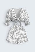 The Saint 54 grey and white toile print two-piece set with a tie-front puff sleeve top and ruffled high-waist shorts.