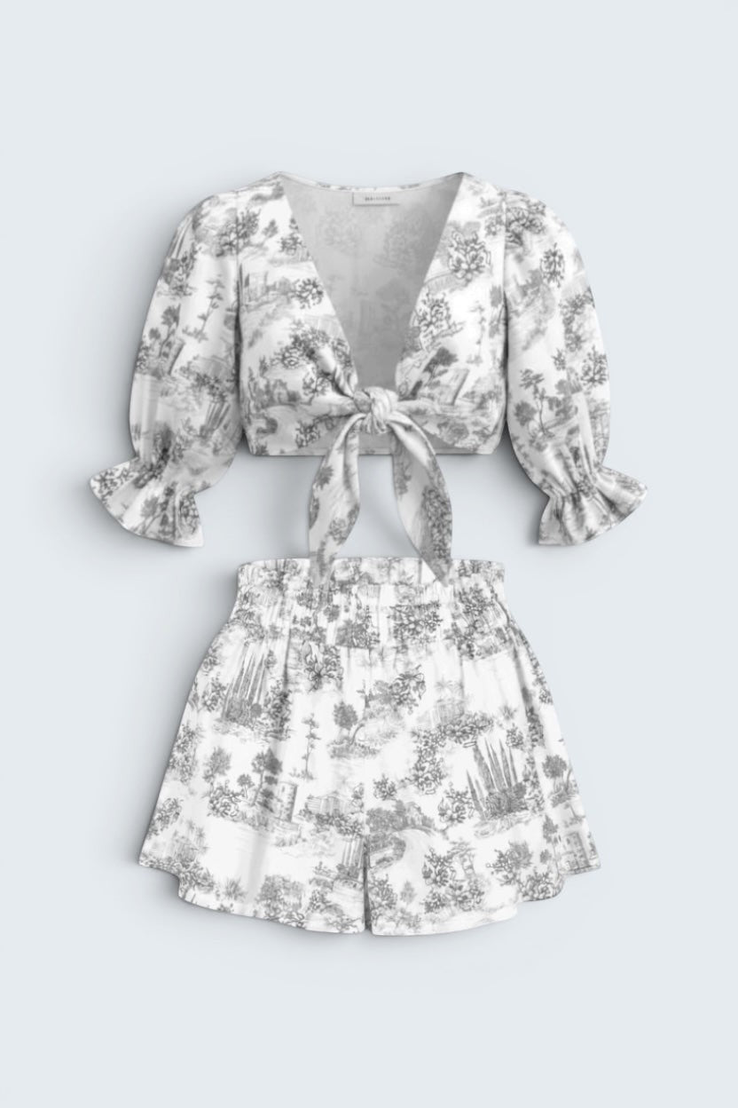 The Saint 54 grey and white toile print two-piece set with a tie-front puff sleeve top and ruffled high-waist shorts.