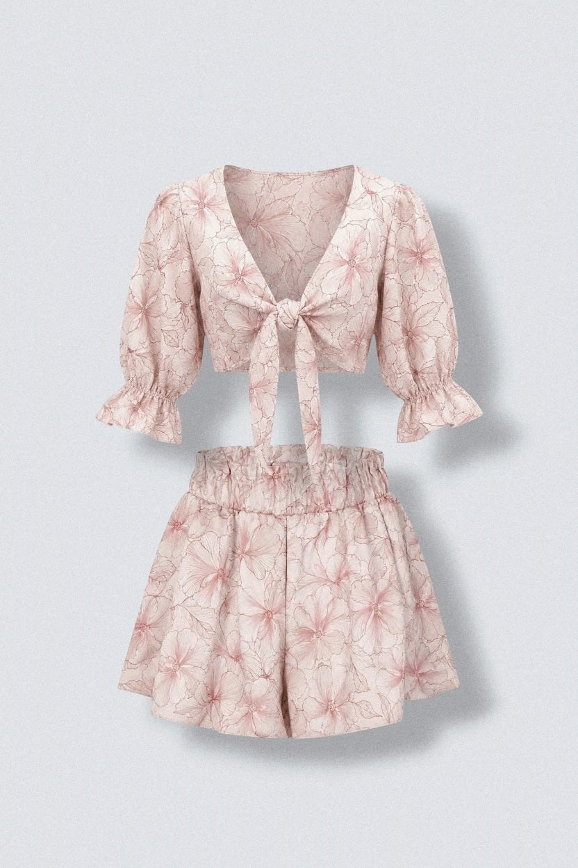 The Saint 54 pink floral print two-piece set featuring a tie-front puff sleeve crop top and ruffled high-waist shorts.