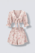 The Saint 54 pink floral print two-piece set featuring a tie-front puff sleeve crop top and ruffled high-waist shorts.